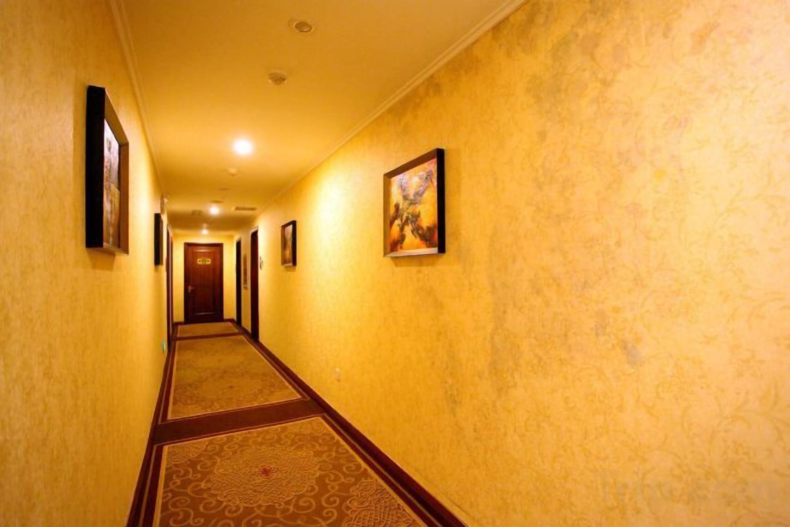 A hallway with patterned carpet, framed artwork on the walls, and a door at the end.