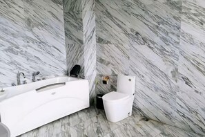 A bathroom with a white bathtub, a toilet, and marble walls.