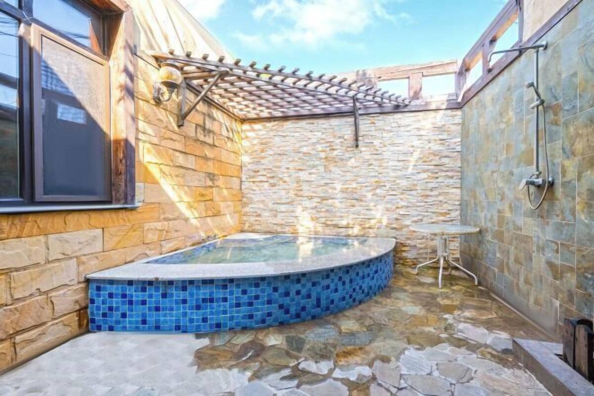 Zona exterior amb parets de pedra, una banyera hidromassatge, una pèrgola i una taula petita.