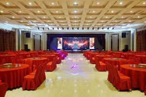 A banquet hall with round tables and chairs, a stage with a large screen, and a ceiling with recessed lighting.