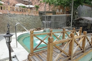Un área de hidromasaje con terraza de madera, pared de piedra y una cascada.