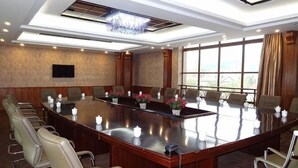 Un salón de conferencias con una larga mesa, sillas, un televisor y ventanas amplias.