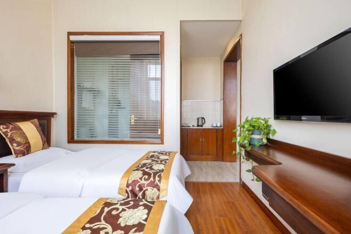Habitació d'hotel amb llit, televisió, una banca de fusta, una planta en test i una zona de cuina equipada.