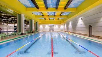 Una piscina interior con separadores de carril bien definidos, un techo con diseño azul y amarillo, y un ambiente luminoso y bien iluminado.
