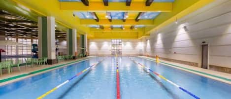 Une piscine intérieure avec des séparateurs de couloirs bien visibles, un plafond aux motifs bleus et jaunes, et un espace lumineux et bien éclairé.