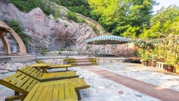 A patio area with wooden benches, a stone pathway, and a view of a rocky hillside.
