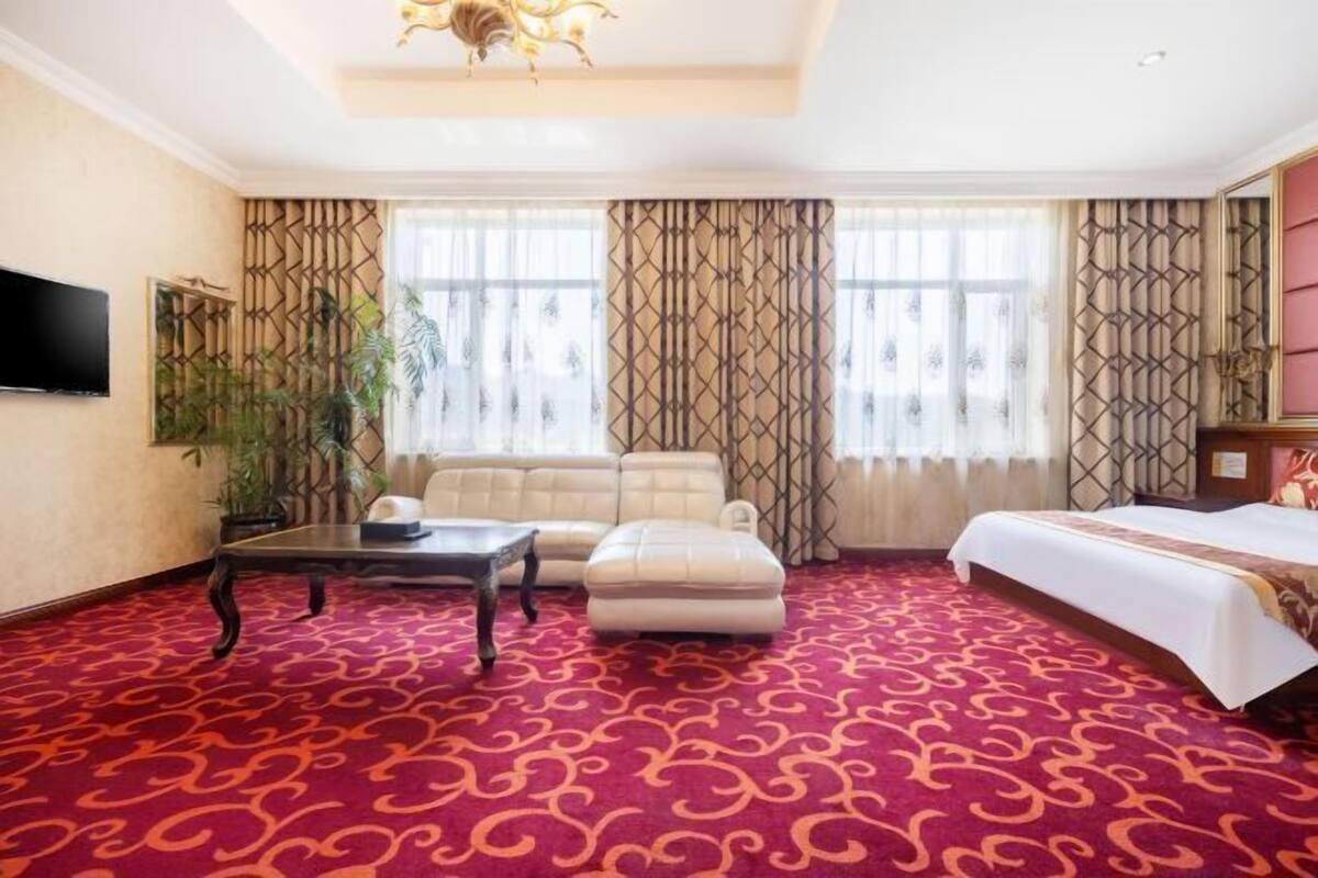 Habitació d'hotel amb un mosaic de moqueta vermell, un sofà, un llit, una televisió i una làmpada decorativa al sostre.