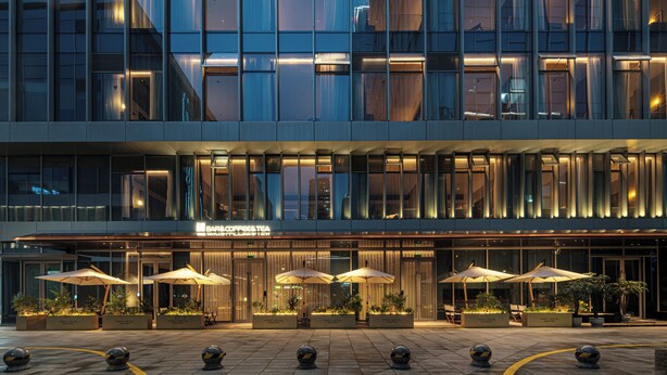 A modern hotel with a glass facade, outdoor seating with umbrellas, and a visible coffee shop. - Hangzhou Tipsy Hotel (Jinsha Lake) (Hangzhou)