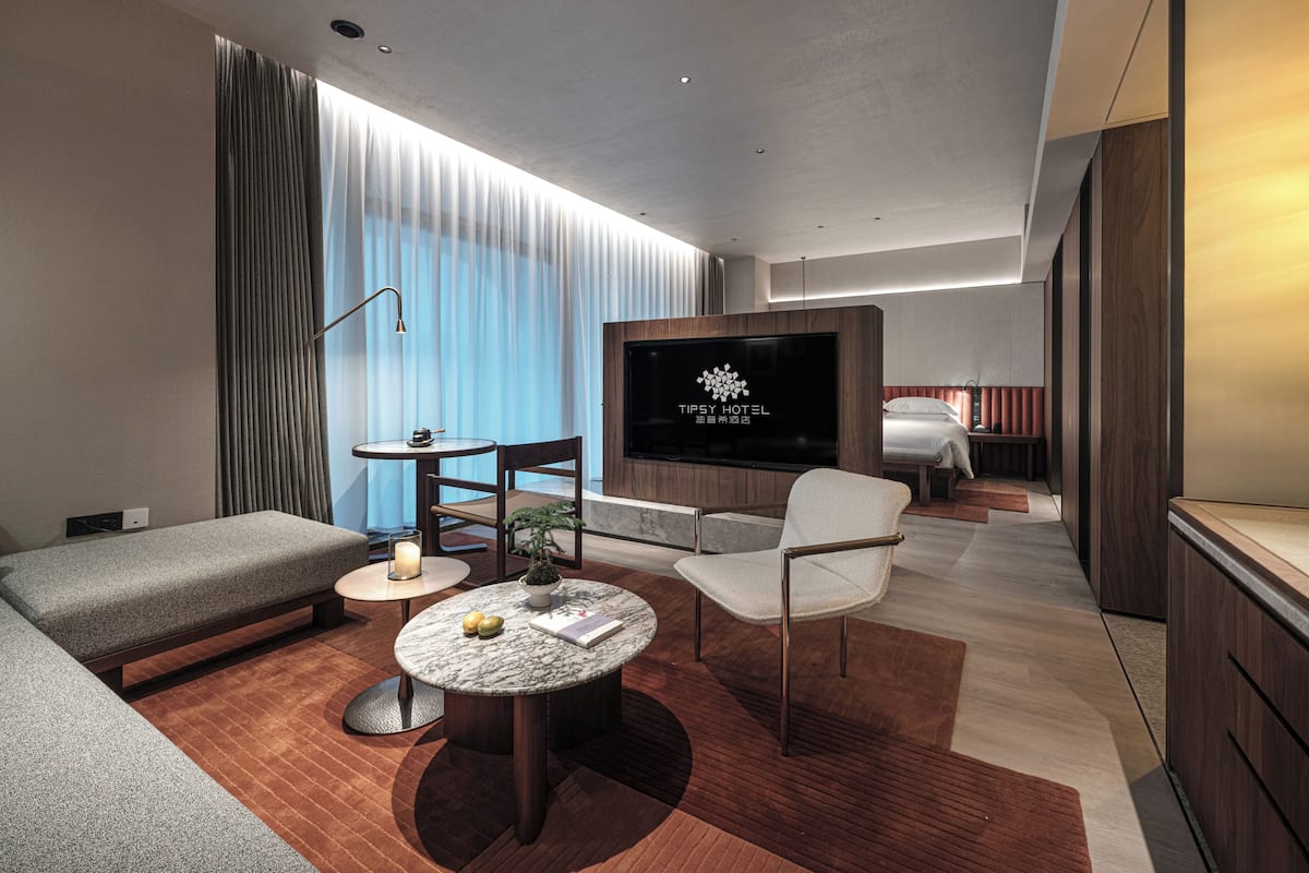 A modern hotel room with a flat-screen TV, a sofa, a chair, a small table, and a bed.