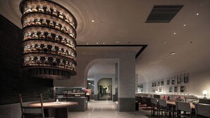 A modern interior with a central column of illuminated bottles, a reception desk, and a seating area with tables and chairs. - Hangzhou Tipsy Hotel (Jinsha Lake) (Hangzhou)