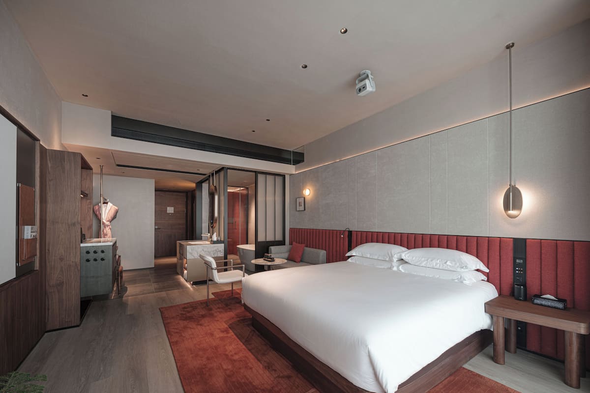 A modern hotel room with a large bed, a desk, a chair, a vanity, and a mirror.