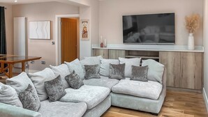 Een woonkamer met een hoekbank, een flatscreen televisie en een houten visgraatvloer.