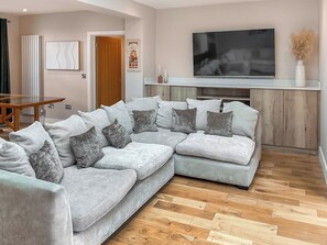 A living room with a sectional sofa, a flat-screen TV, and a wooden herringbone floor. - 4 bedroom accommodation in Ringwood (Ringwood)