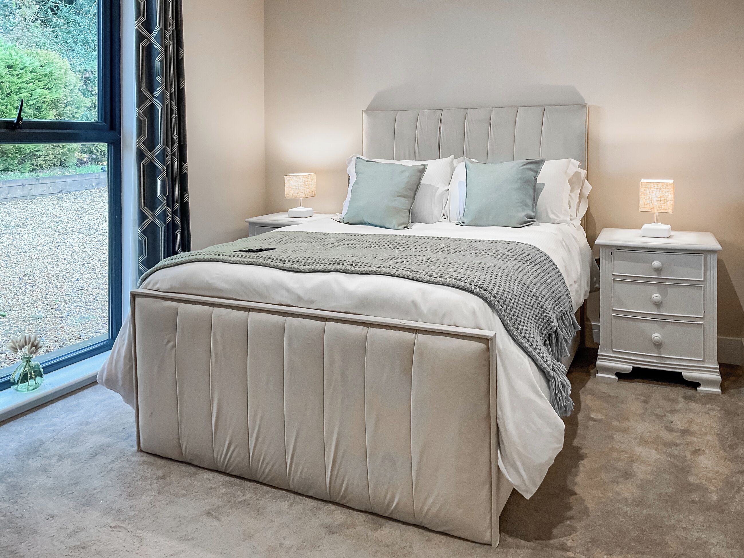 A bedroom with a bed, bedside tables, a window, and a view of greenery outside.