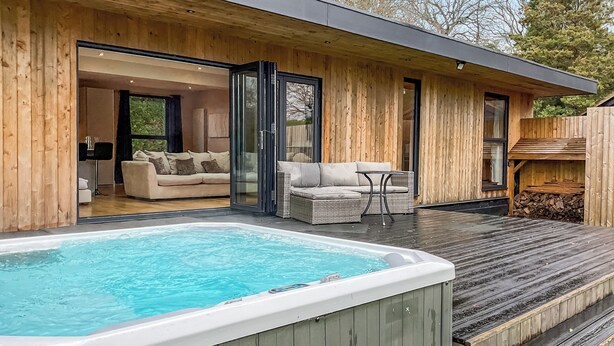 Een houten terras met een jacuzzi, een bank en een tafel.