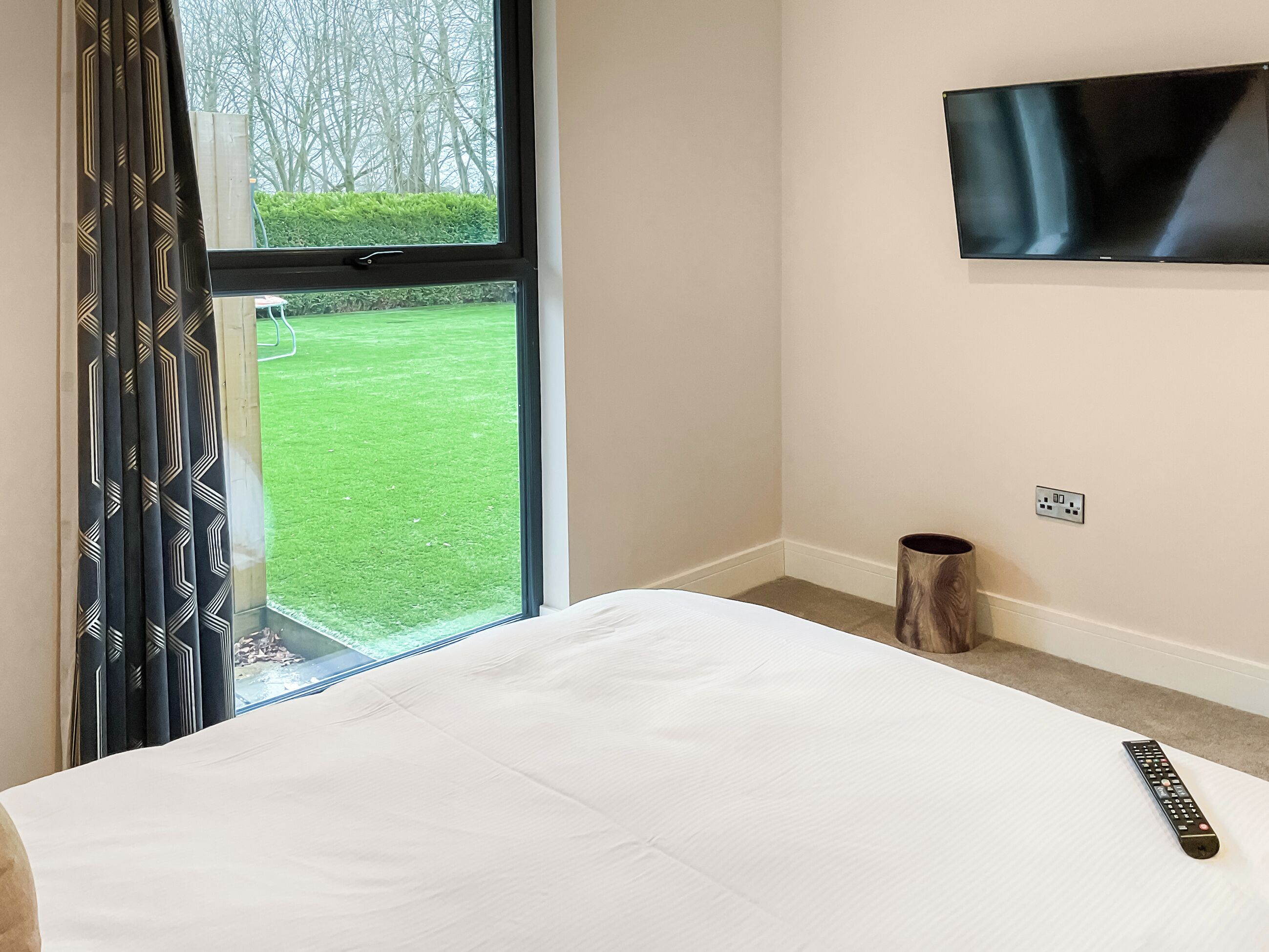 Ein Hotelzimmer mit Bett, Wand-Fernseher, Fenster mit Vorhängen und einer kleinen Mülltonne.