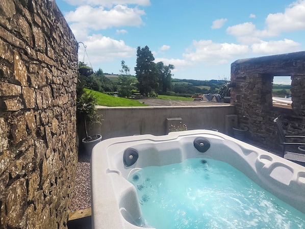 Un bain à remous avec vue sur un mur de pierres et un paysage verdoyant.