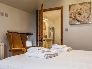 Une chambre d’hôtel avec un lit, une chaise, une salle de bain visible à travers une porte ouverte et un tableau accroché au mur.