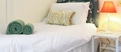 A neatly made bed with white linens, a green headboard, and a bedside table with a lamp and a book shelf.