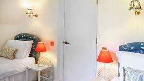 Ett rum med två sängar, var och en med en vit sänggavel, ett litet vitt sidobord och en röd lampa. Det finns en vit dörr i mitten.