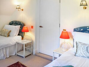 A room with two beds, each with a white headboard, a small white side table, and a red lamp. There is a white door in the center. - 3 bedroom accommodation in Near Bath (Bradford-on-Avon)