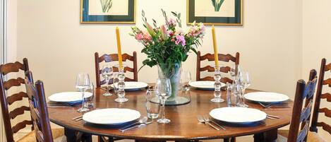 A dining table set for six with chairs, a vase with flowers, and framed botanical prints on the wall.