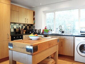 A modern kitchen with wooden cabinets, a built-in dishwasher, and a large window providing natural light. - 3 bedroom accommodation in Near Bath (Bradford-on-Avon)