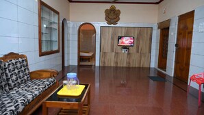 A hotel lobby with a sofa, a small table with a bottle and glass, a television, and a ceiling fan.