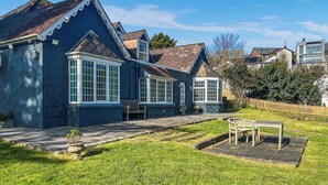 A residential property with a large front yard, a wooden bench, and a paved patio area. - 5 bedroom accommodation in Perranporth (Perranporth)