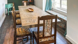 A dining area with a wooden table, chairs, a bench, and a window with curtains. - 5 bedroom accommodation in Perranporth (Perranporth)