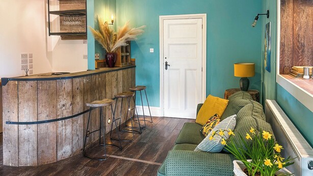 A cozy interior with a wooden bar area, a green sofa with yellow flowers, and a door. - 5 bedroom accommodation in Perranporth (Perranporth)
