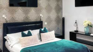 Ein modernes Schlafzimmer mit einem Bett, einem Nachttisch, einer Vase mit Blumen und einem an der Wand befestigten Fernseher.