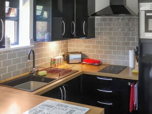 Uma cozinha com armários pretos, uma pia de aço inoxidável, uma torradeira e um eletrodoméstico vermelho na bancada.