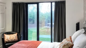 Un dormitorio con cama, una silla, televisor y puerta corrediza de vidrio que da a un jardín.