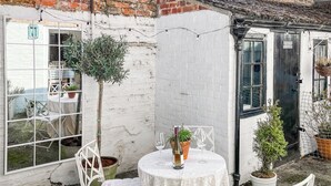 A small outdoor seating area with a table and chairs, a potted plant, and a brick wall.