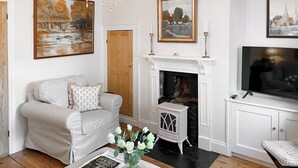 A living room with a fireplace, a sofa, a coffee table with a magazine and vase, and a TV on a cabinet.