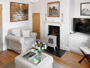 Una sala de estar con chimenea, un sofá, una mesa de centro con una revista y un jarrón, y un televisor sobre un mueble.