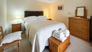 A neatly made bed with white linens, a wooden nightstand with a lamp, a wooden dresser with a mirror, and a chair with a pillow. - 1 bedroom accommodation in Portree (Portree)