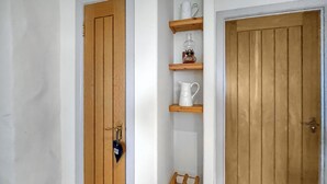 A hallway with wooden doors, a white wall, and a wooden shelf with a white pitcher and a glass bottle. - 1 bedroom accommodation in Portree (Portree)