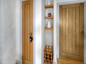 Ein Flur mit Holztüren, einer weißen Wand und einem Holzregal mit einer weißen Krug und einer Glasflasche.