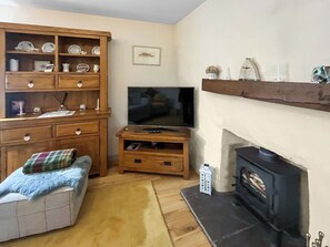 A living room with a wooden entertainment unit, a flat-screen TV, a fireplace, and a small seating area. - 1 bedroom accommodation in Portree (Portree)
