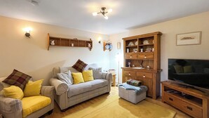 A living room with a sofa, ottoman, wooden cabinet, and a television. - 1 bedroom accommodation in Portree (Portree)
