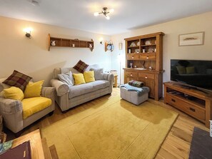 Ein Wohnzimmer mit einer Couch, einem Hocker, einem Holzschrank und einem Fernseher.
