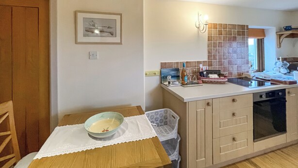 A kitchen with a tiled backsplash, a sink, a countertop, and a dining table with a bowl. - 1 bedroom accommodation in Portree (Portree)