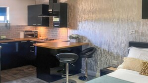 Una cocina compacta con una isla central, taburetes de bar, una cama con cabecera y una pared con textura.