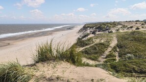 Une plage avec des dunes, un ciel dégagé et l’océan.