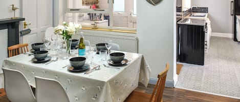 Ein Essbereich mit einem Tisch für vier Personen, Stühlen, einer Vase mit Blumen und Blick zur Küche.