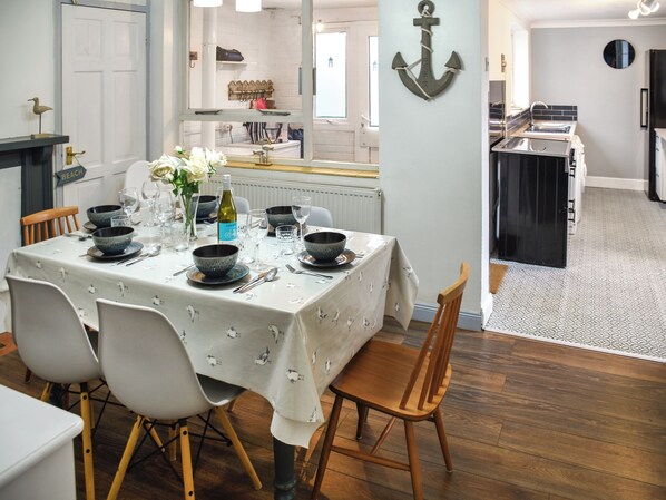 Un comedor con una mesa dispuesta para cuatro, sillas, un florero con flores y vistas a la cocina.