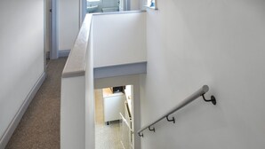 Escadaria com corrimão, degraus carpetados e vista para um espaço com cozinha.