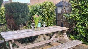 A wooden picnic table with a vase of pink flowers and two wine glasses. - 1 bedroom accommodation in Kelbrook (Kelbrook)